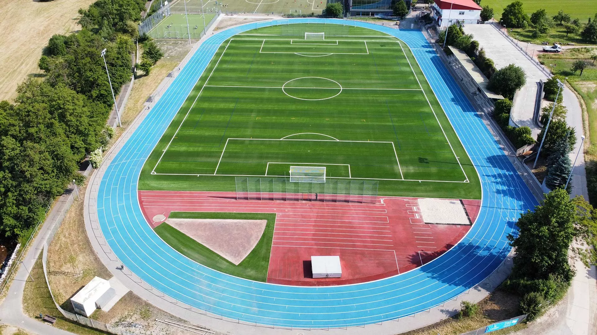 Luftaufnahme einer modernen Sportanlage mit Kunstrasen-Spielfeld und Kunststofflaufbahn